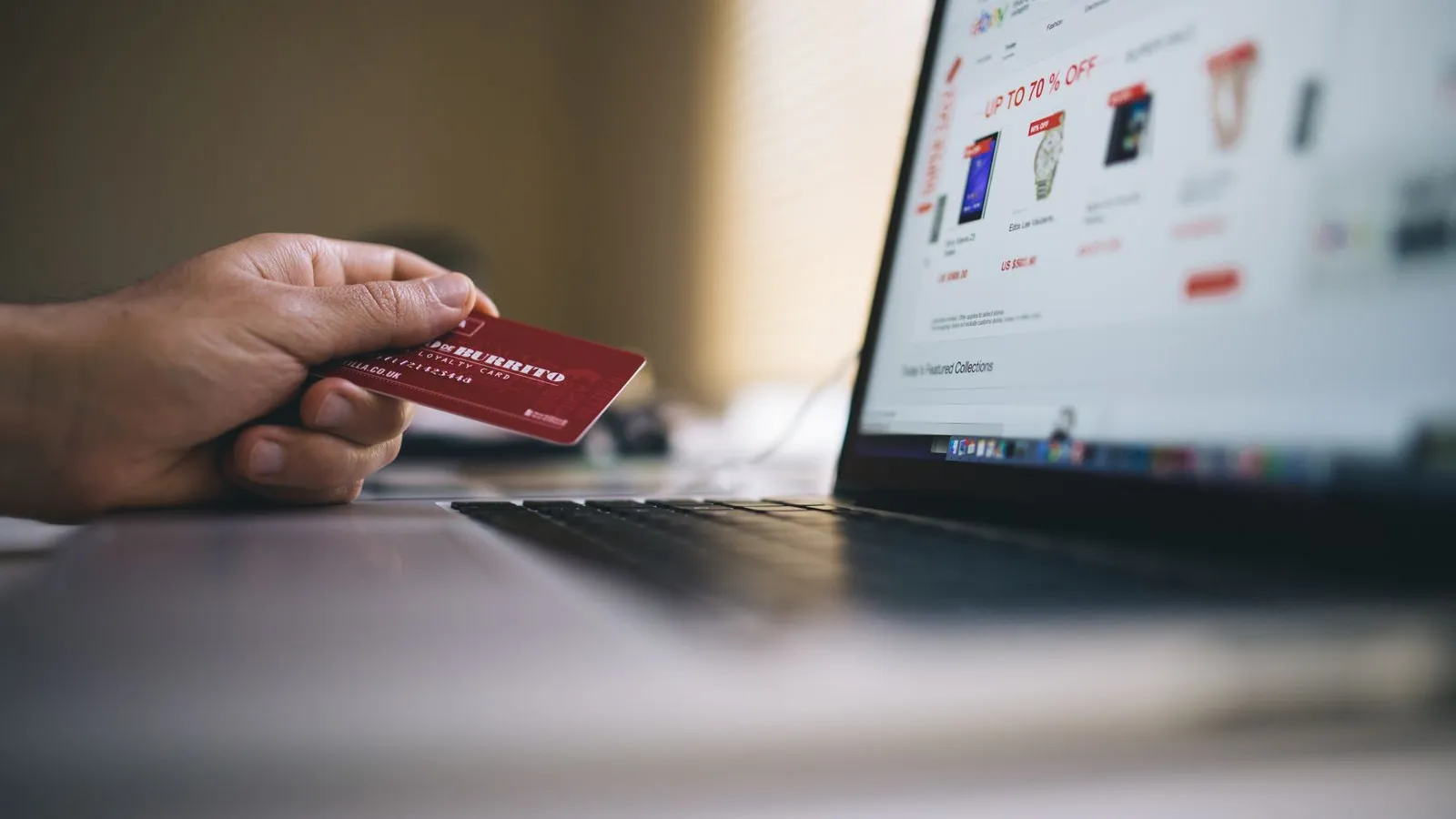 A hand holding a payment card in front of a laptop showing an online shop