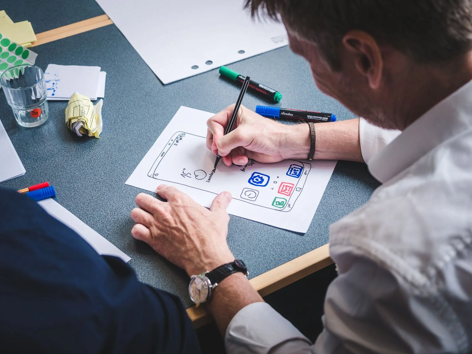 A designer sketches a mobile app screen with icons on paper during a UX workshop