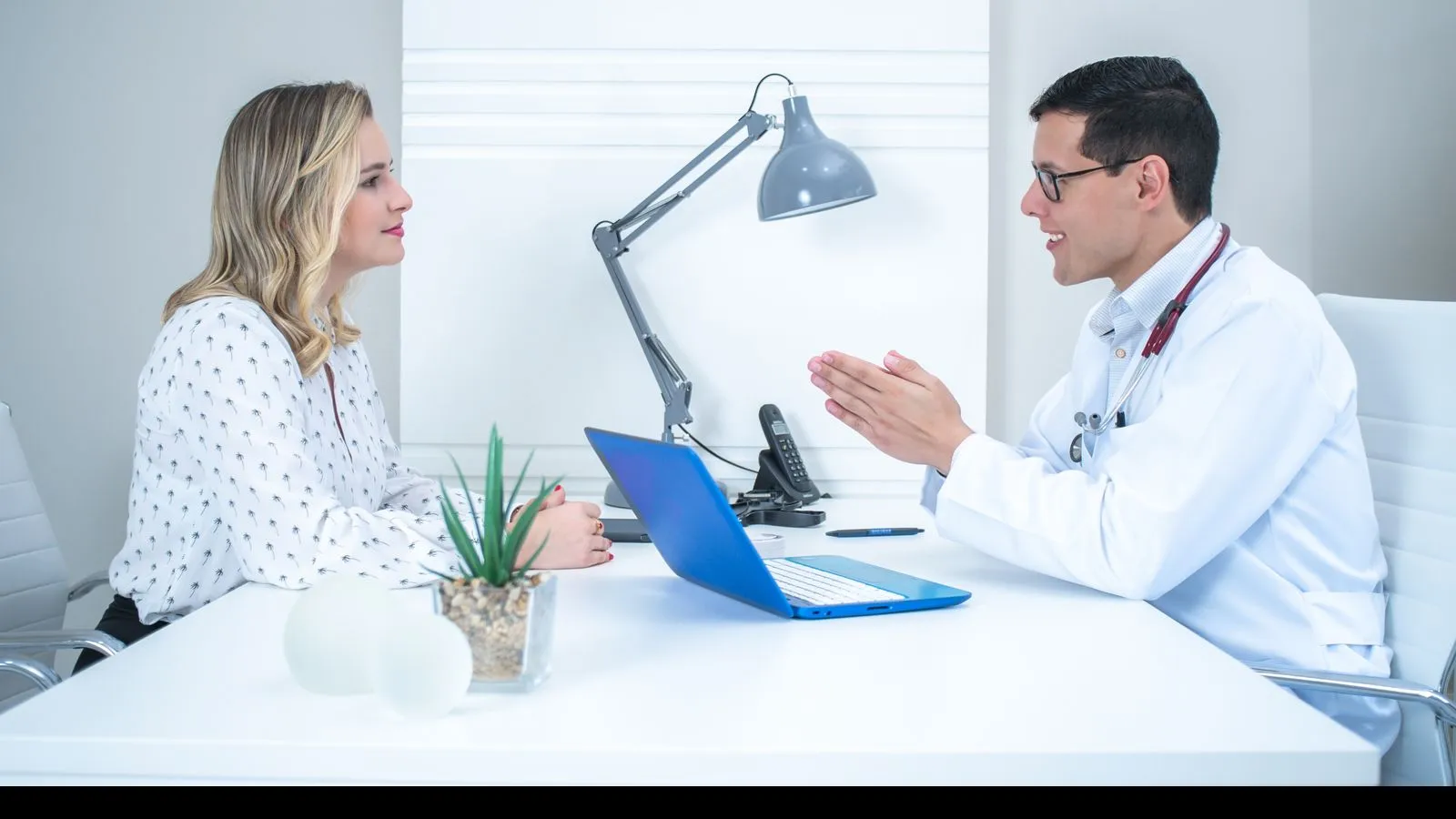 A doctor talks with a patient at a desk with a laptop