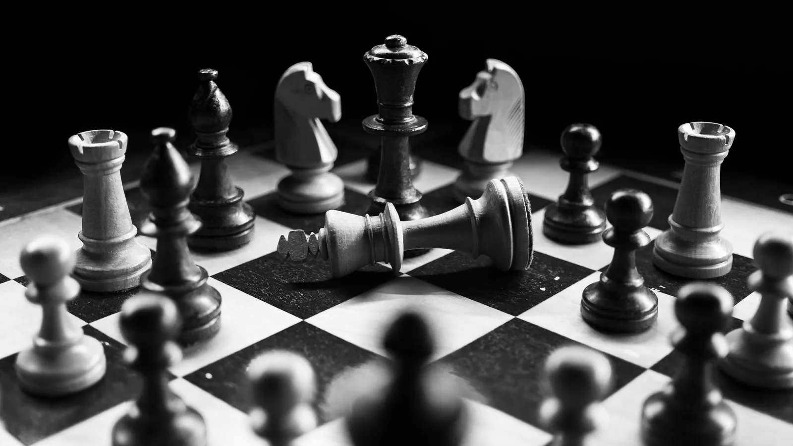 Black and white chess pieces on a board, with a toppled king