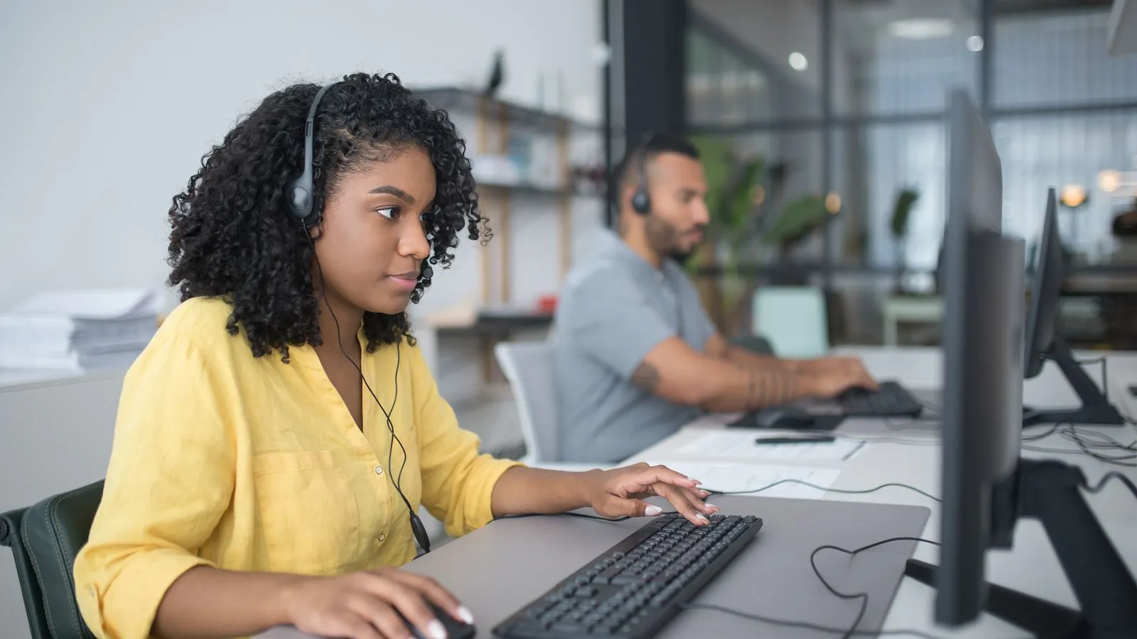 A customer service agent with a headset works at a computer in a contact center