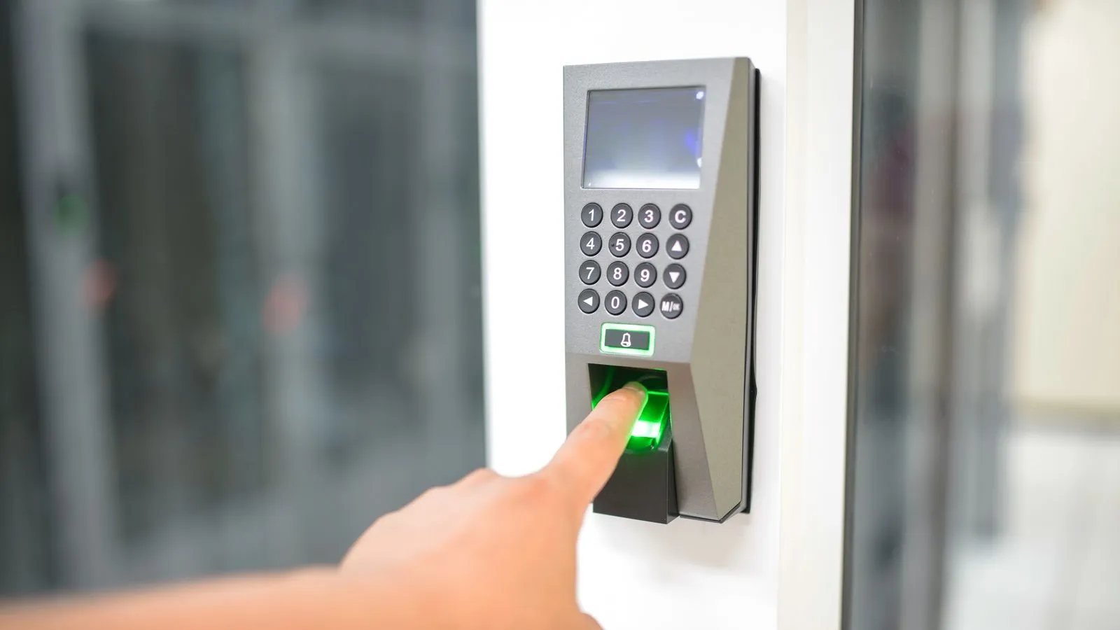 A finger pressed on a fingerprint scanner next to a keypad on a door