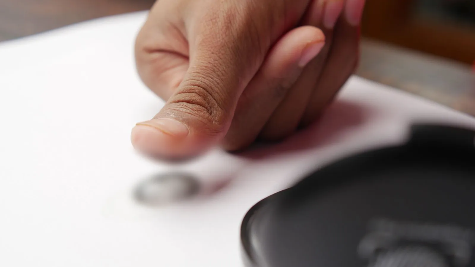 A thumb next to an inked fingerprint on paper, with the print and the thumb pad blurred