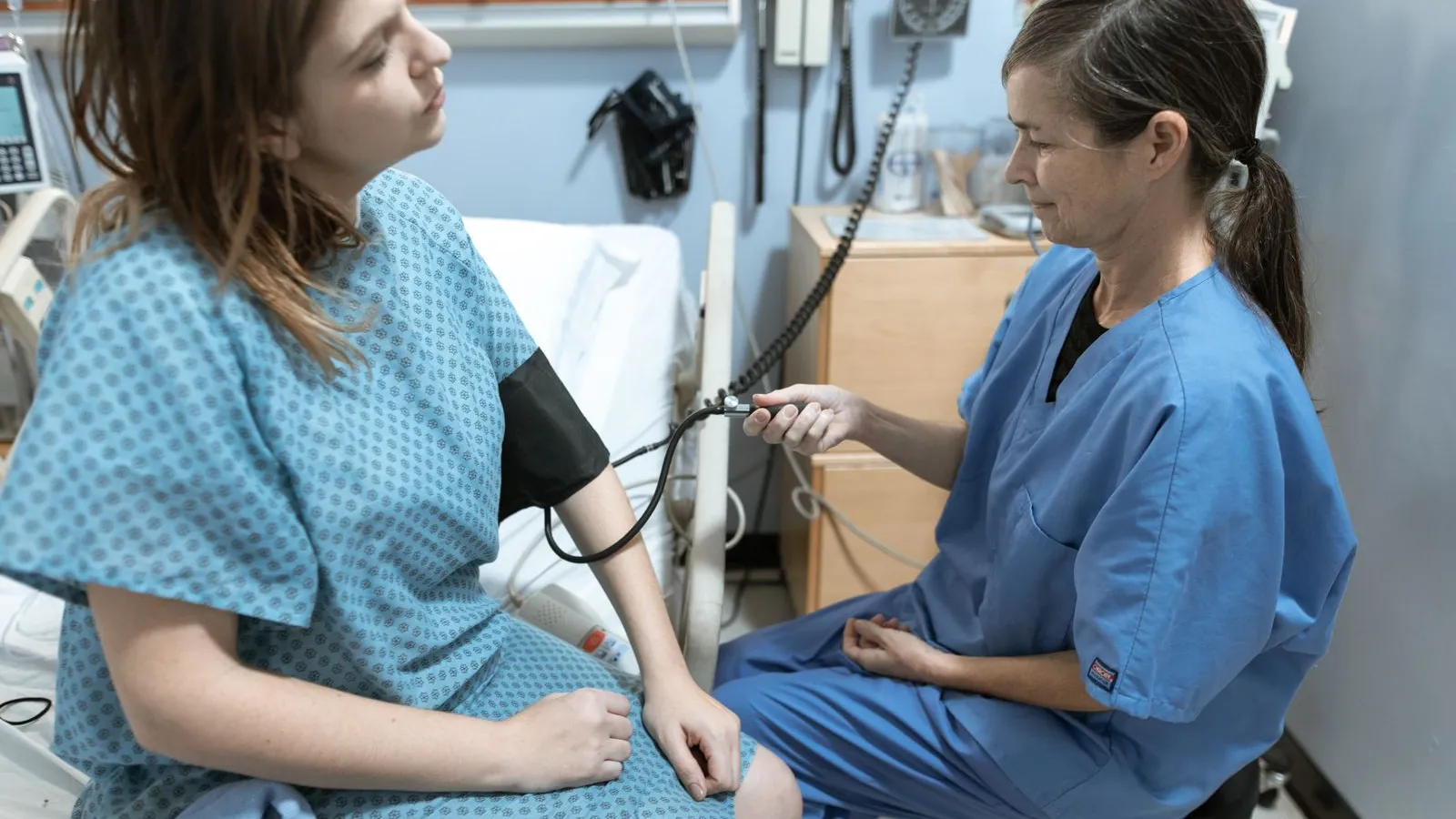 A nurse in blue scrubs taking a patient blood pressure in a clinic