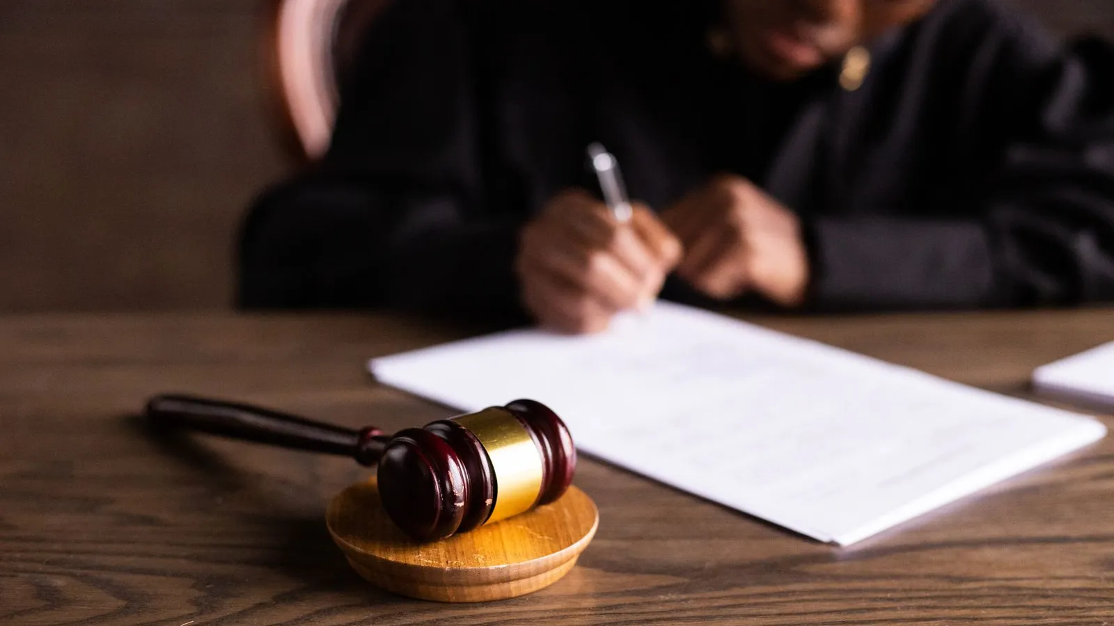 A judge writing at a desk with a gavel in the foreground