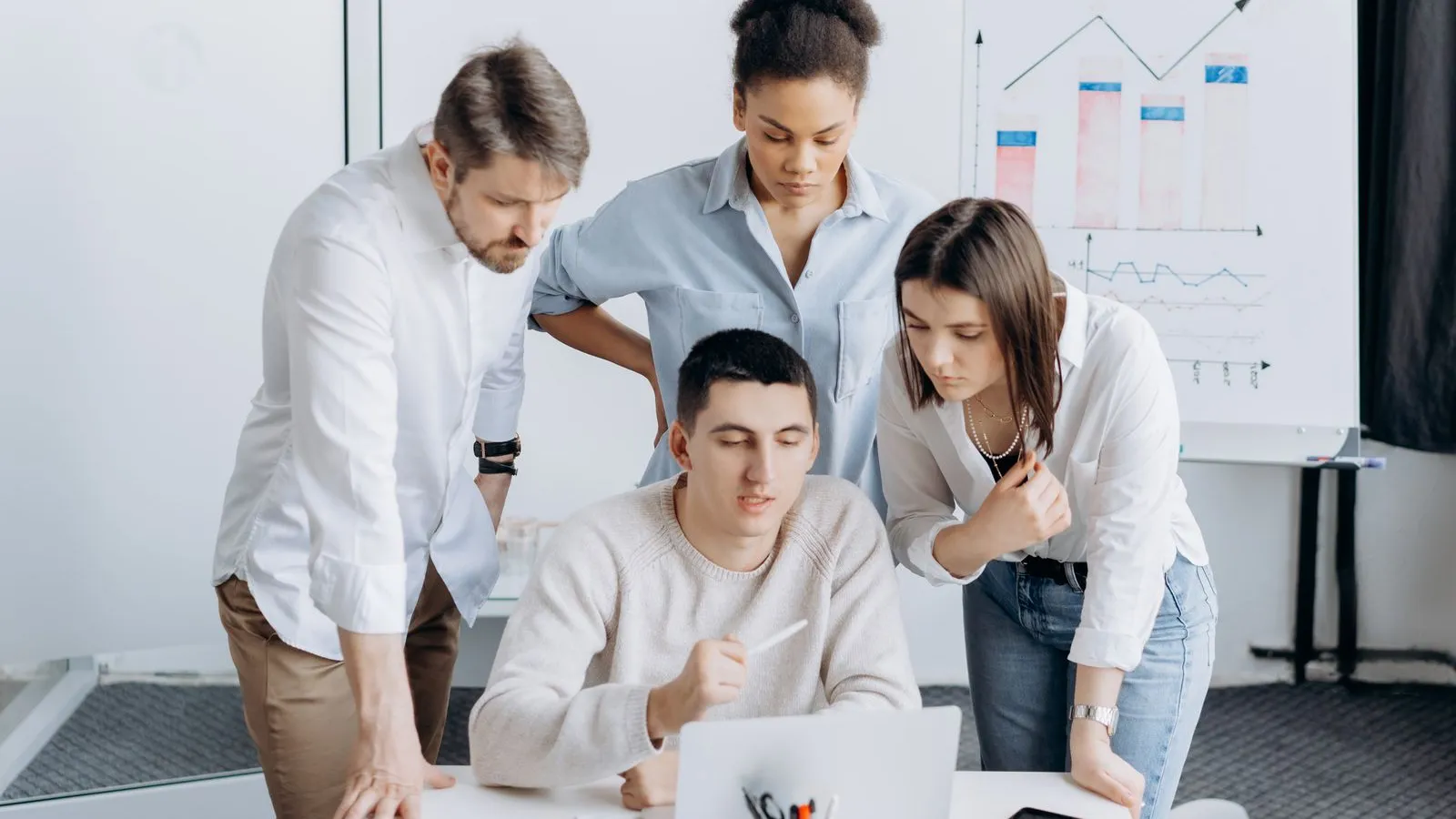A marketing team reviewing results on a laptop in front of a whiteboard with charts