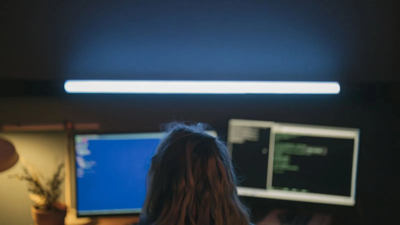 Developer at a desk with two monitors in a dim room, testing code